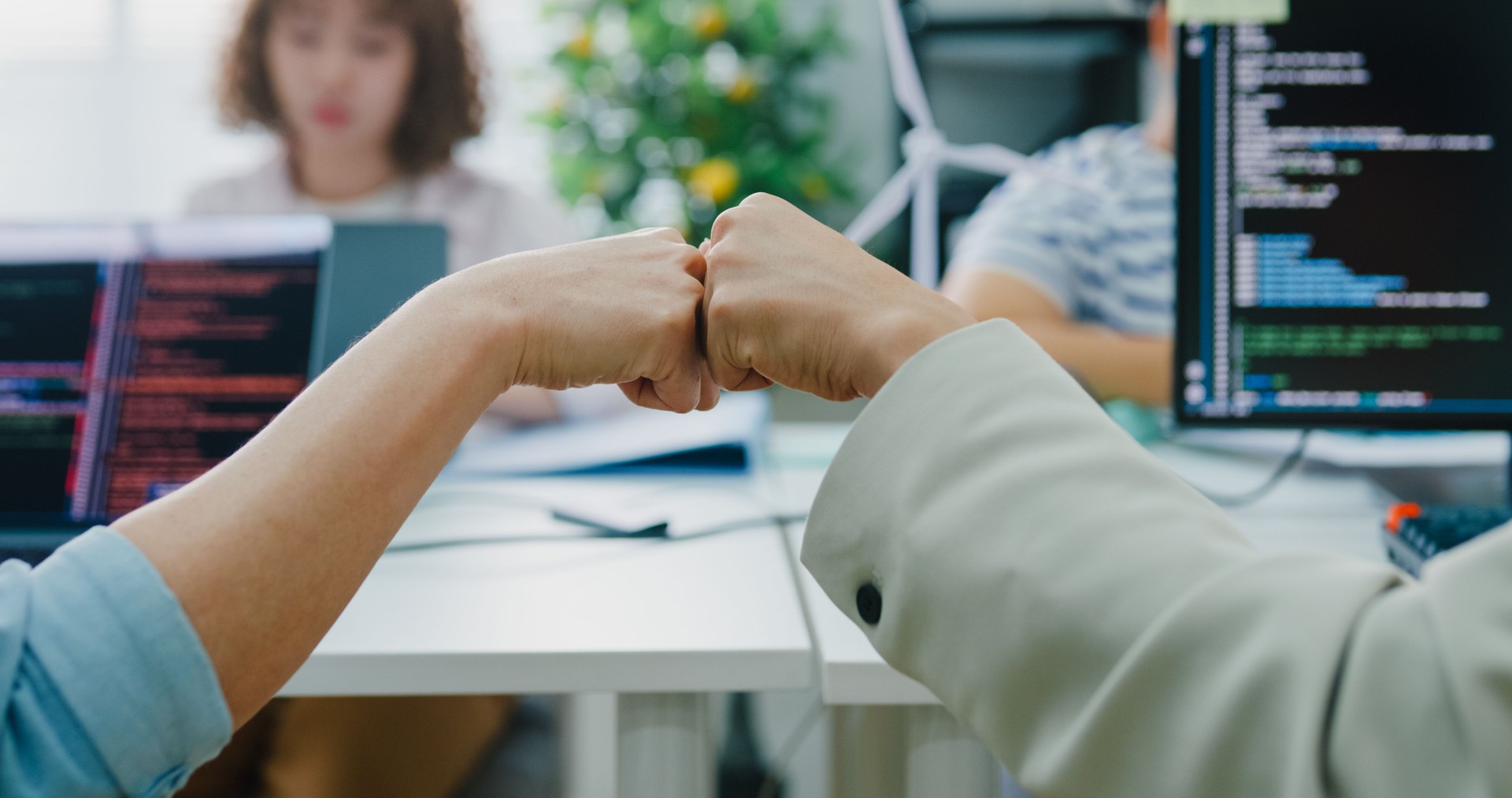 Closeup of Asian colleagues LGBTQIA+ community, share a moment of success with a fist bump, while a focused team works of their sustainable business office. ESG sustainable business office.